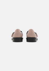 Pantofi din piele roz cu talpă neagră, având un design cu spate deschis și detalii cu cataramă. Textură netedă și stil minimalist.
