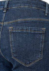 Tmavomodré džínsy vyrobené z denimu, ktoré obsahujú zadné vrecko s špicatou klopou a jemnými švovými detailmi. Tkanina má hladkú štruktúru.