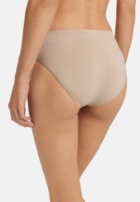 Beige korkean vyötärön alushousut, jotka on valmistettu sileästä kankaasta, saumattomalla muotoilulla ja huomaamattomalla ompelulla vyötärönauhan ja lahkeiden reunoilla.
