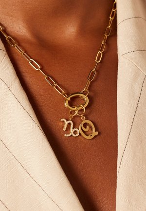 Goldkette mit ovalen Gliedern, die zwei Anhänger aufweist: einer ist mit Strasssteinen besetzt, der andere hat ein Schriftzug-Design.
