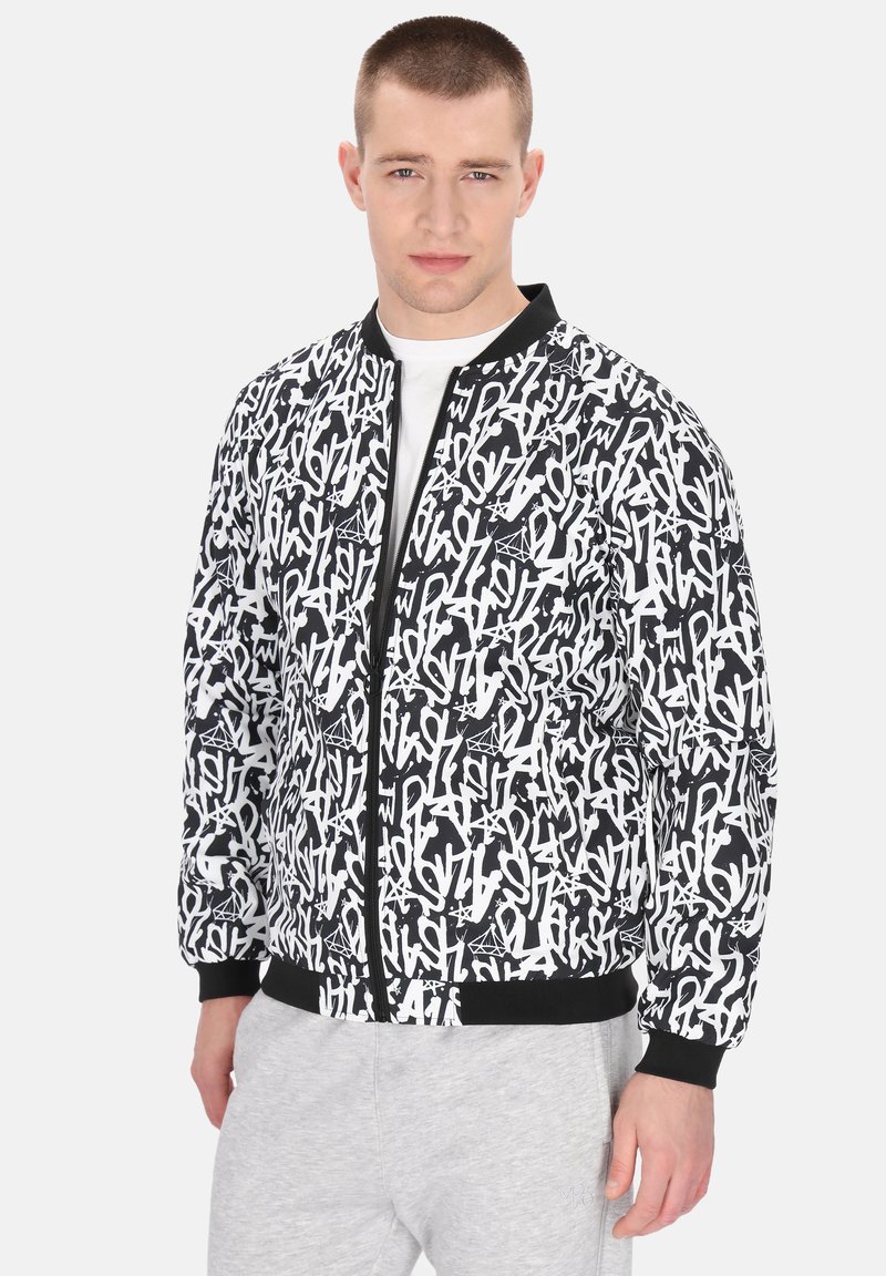 Svart och vit bomberjacka med ett grafiskt textmönster, ribbade mudd och fåll, samt en framzipper. Bärs över en vit skjorta.