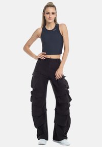 Merkkitön sininen ilmanhiha crop-top, joka on yhdistetty löysiin mustiin cargo-housuihin, joissa on useita suureita taskuja ja kerroksellisia paneeleita. Valkoiset lenkkarit mukana.