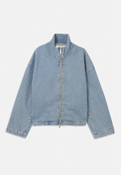 Heled sinine teksajakk kõrge kaelusega, ees luku sulgemine ja lahtiste, pikkade varrukatega. Omab lihtsat disaini ja minimaalset detailirohkust.