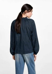 Marinblus med strukturerat mönster, lös passform, rynkad halsringning och långa ärmar. I kombination med ljusblå, avslappnade jeans.