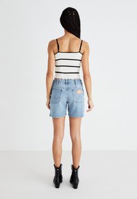 Μπλε τζιν σορτσάκι με ψηλή μέση, γυριστό στρίφωμα και πίσω τσέπες; συνδυασμένο με λευκό και μαύρο ριγέ αμάνικο μπλουζάκι. Μαύρες μποτάκια μέχρι τον αστράγαλο.