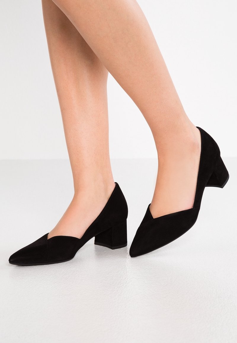 Chaussures à talon bas en daim noir avec bout pointu et découpe en forme de V sur les côtés, présentant une texture lisse et un design structuré.
