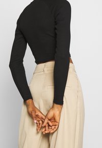 Černý žebrovaný dlouhý rukáv cropped top v kombinaci s béžovými kalhotami s vysokým pasem, které ukazují texturovanou látku a propracované designové detaily.
