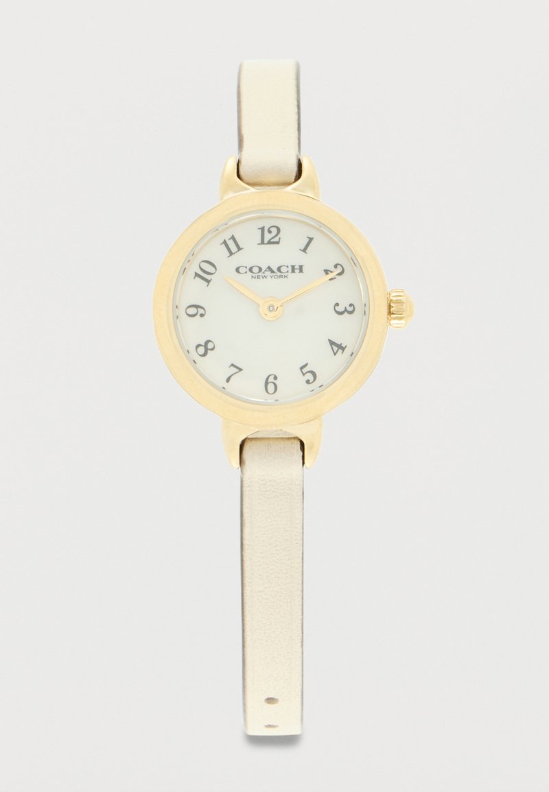 Στρογγυλό ρολόι χειρός Coach σε χρυσό χρώμα με λευκό καντράν, μαύρους αριθμούς, δύο δείκτες και στενό μπεζ δερμάτινο λουράκι.