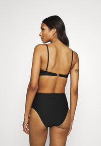 Black high-waisted bikini bottoms with ribbed texture, paired with a matching top featuring thin adjustable straps and a clasp closure.