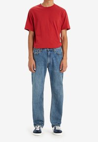 Czerwona bawełniana koszulka zestawiona z jasnoniebieskimi, prostymi dżinsami. Strój uzupełniają granatowe trampki z białymi sznurowadłami.