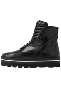 Botas altas de cuero negras con lengüeta acolchada, acabado texturizado, detalles en blanco en la suela y un diseño de suela gruesa y con tacos.