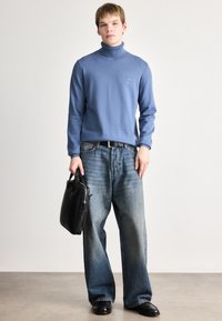 Suéter de gola alta azul clara, jeans de denim desbotado de corte relaxado, bolsa de couro preta, sapatos pretos. Design simples e textura suave em toda a peça.