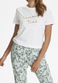 Bílý bavlněný tričko s nápisem "Letní čas" ve zlatém písmu, v kombinaci s vzorovanými kalhotami v zelené a modré květinové designu.
