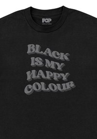 Camiseta de algodón negra con cuello redondo, que presenta un gran diseño de texto en 3D en gris que dice "EL NEGRO ES MI COLOR FELIZ." Textura suave.