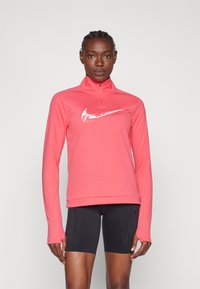 Ružičasta duguga sportska majica s polu-zip ovratnikom i bijelim logotipom. Izrađena od glatkog, rastezljivog materijala, u kombinaciji s crnim priljubljenim šortsevima.