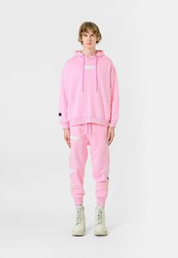 Sudadera rosa con cordones, combinada con joggers rosas que presentan acentos decorativos. Botas de combate blancas completan el conjunto.