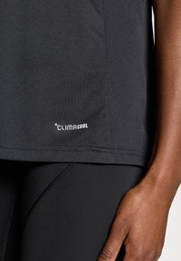 Μαύρο αθλητικό πουκάμισο με υφή, που φέρει λευκό λογότυπο "CLIMACOOL" κοντά στο τελείωμα. Συνδυάζεται με μαύρο κολάν.