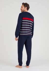 Marineblauwe top met lange mouwen en een rode horizontale streep, met meerkleurige strepen. Combinatie met marineblauwe broek, die een casual, ontspannen pasvorm toont.