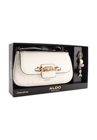 Biała torba na ramię z złotymi dodatkami, tłoczonym wzorem, łańcuszkiem na klapce oraz dopasowanym brelokiem z różnymi zawieszkami.