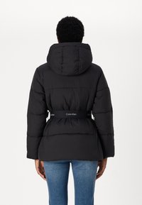 Black puffer jacket with a hood, featuring a belted waist and signature band. Thick, quilted design with a matte finish.