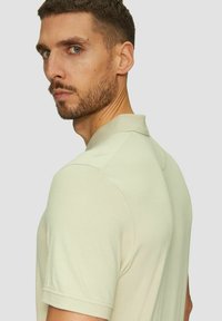 Polohemd in hellbeige, aus strukturiertem Stoff mit klassischem Kragen und kurzen Ärmeln. Verfügt über subtile Stichdetails.