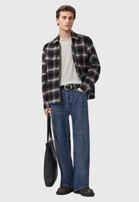 Camicia a quadri bianco e nero, t-shirt grigia, jeans azzurri larghi, cintura nera, borsa nera e scarpe nere. Outfit casual in taglio comodo.