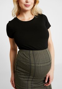 Top nero a maniche corte abbinato a una gonna verde a scacchi aderente con una fascia elastica in vita per un maggiore comfort.