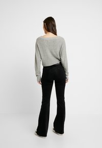 Grå, stickad tröja med lös passform och bred halsringning, kombinerad med svarta, utsvängda kordbyxor. Båda plaggen har en slät textur.