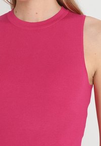 Top sin mangas de canalé ajustado en un vibrante color rosa, con cuello redondo, que destaca por su textura suave y tejido elástico.