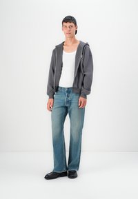 Gray zip-up hoodie, white tank top, light blue straight-leg jeans, and black shoes. Smooth fabric, relaxed fit, minimal design.