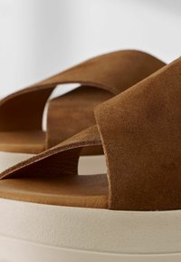 Sandali in suede marrone con un design a doppia fascia, caratterizzati da una superficie testurizzata e una leggera suola piattaforma bianca.
