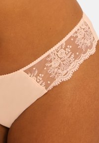 Sous-vêtements roses avec un bord en dentelle, ornés de détails floraux transparents sur la ceinture. Le tissu principal est lisse avec une finition mate.