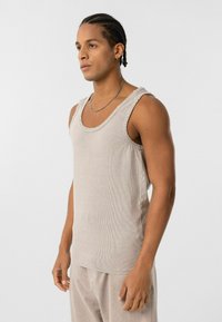 Beige mouwloze geribbelde tanktop met rafelige randen en een ronde halslijn, gecombineerd met lichtgekleurde broeken. Glad oppervlak, casual ontwerp.