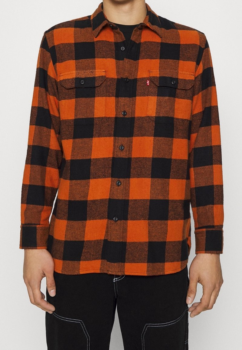 Chemise en flanelle rouge et noire à carreaux avec manches longues, deux poches poitrine, fermeture à boutons et tissu texturé. Dotée d'un col.