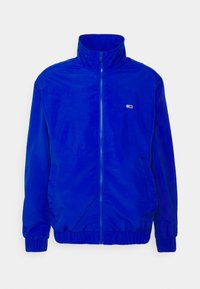 Blue zip-up jacket made of smooth fabric, featuring a high collar, elastic cuffs, and side pockets. Small logo accent on the chest.