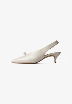 Beige leren slingback kitten heel schoen met spitse neus en decoratieve ronde parel bovenop, tegen een witte achtergrond.