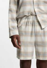 Leichtes karriertes Schlafanzugset mit einem Muster aus Grau, Beige und Weiß. Das Shirt hat eine lässige Passform mit einer Knopfverschluss; die Shorts verfügen über einen elastischen Bund.
