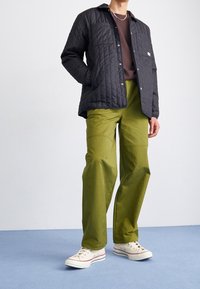 Czarna pikowana kurtka, zielone spodnie z kieszeniami i białe tenisówki. Prosty fason, lekka tkanina i kontrastujące kolory.