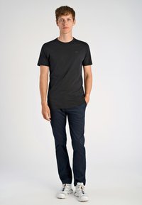 Mustat lyhyet hihat T-paita, jossa on pyöreä kaula-aukko ja hillitty logo, yhdistettynä tummansinisiin housuihin ja valkoisiin urheilukenkien kanssa, joissa on värikkäät nauhat.