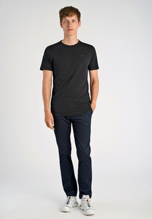 Zwarte korte mouwen t-shirt met een ronde halslijn en een subtiele logo, gecombineerd met marineblauwe broek en witte sportschoenen met kleurrijke veters.