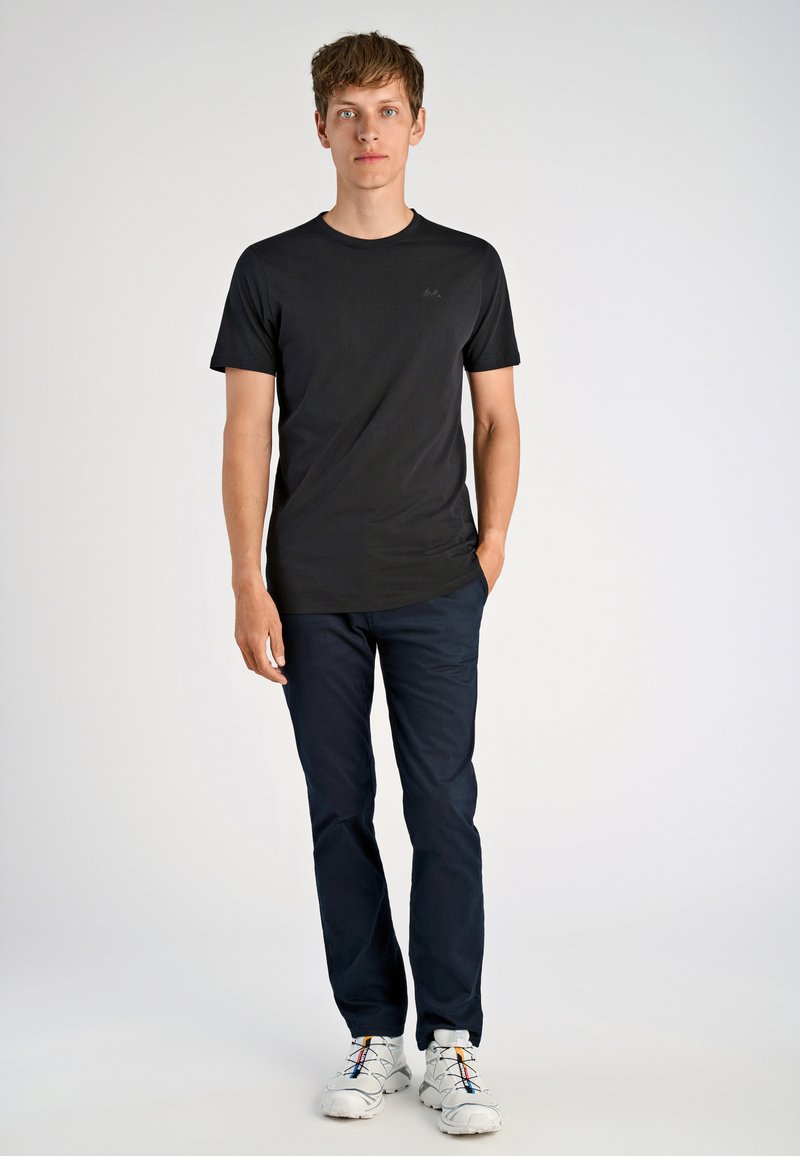 Mustat lyhyet hihat T-paita, jossa on pyöreä kaula-aukko ja hillitty logo, yhdistettynä tummansinisiin housuihin ja valkoisiin urheilukenkien kanssa, joissa on värikkäät nauhat.