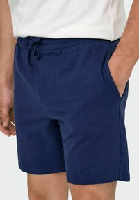 Pantalones cortos azul marino con un patrón texturizado, que cuentan con una cintura con cordón y bolsillos laterales. El material es ligero y transpirable.