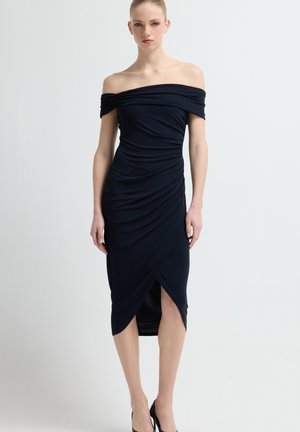 Marineblå kjole med bare skuldre lavet af blødt stof, med rynkede detaljer og et slids op til låret. Figurformet design med en lige kant.