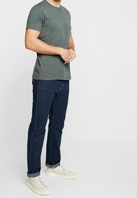 Graues T-Shirt mit kurzen Ärmeln, kombiniert mit dunkelblauen Jeans und hellen Sneakern. Das T-Shirt hat einen Rundhalsausschnitt und eine schlanke Passform.
