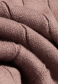 Tissu tricoté rose poudré doux avec des mailles visibles, plié de près pour montrer la texture et l'épaisseur du matériau.