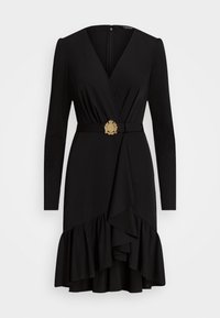 Svart omslagsklänning med långa ärmar, en volangkant och en dekorativ guldspänne. Slät tyg med en figurnära design.