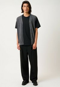 Chaqueta de punto gris con botones sobre una camiseta negra, combinada con pantalones negros holgados y calzado negro. Textura suave, diseño casual.