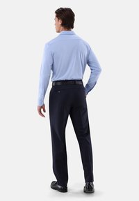 Camicia a maniche lunghe azzurro chiaro con colletto aperto, abbinata a pantaloni blu scuro. Presenta una texture liscia e una cintura nera, con cuciture sottili.