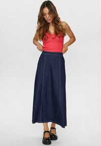 Denim maksi svārki ar vidēju vidukļa augstumu, tumši zila krāsa, smalkas šuvju detaļas un plūstoša dizaina apvienojums ar pieguļošu sarkanu topu.
