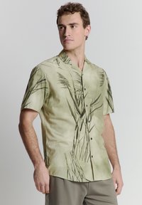 Korte mouw shirt in lichtgroen met een donkergroen plantenpatroon, gemaakt van een gladde stof. Heeft een notch-kraag en knopen aan de voorkant.